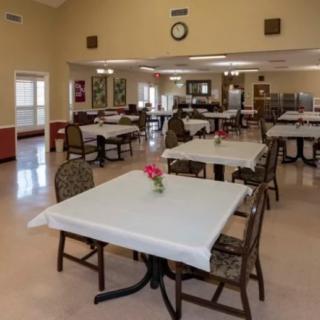 An empty dining hall with tables and chairs neatly arranged, featuring floral centerpieces.