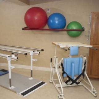 A physical therapy room equipped with therapy balls, parallel bars, and a standing frame.