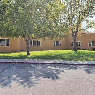 A single-story building with trees and grass in front, viewed from across the road.