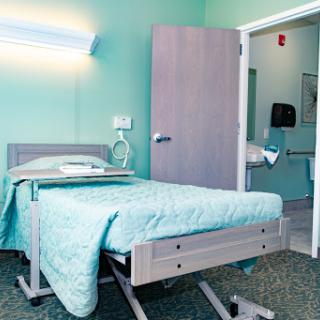 A view of a hospital patient room featuring a hospital bed and calming green walls.