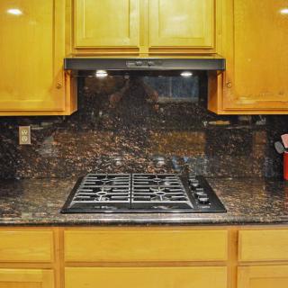 A kitchen with a gas stovetop, wooden cabinets, and a granite backsplash.