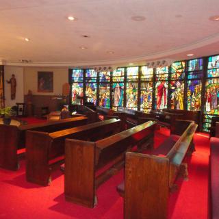 Interior view of a chapel featuring wooden pews and vibrant stained glass windows.