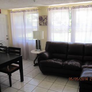 A cozy living room with a sofa, dining table, and large windows.
