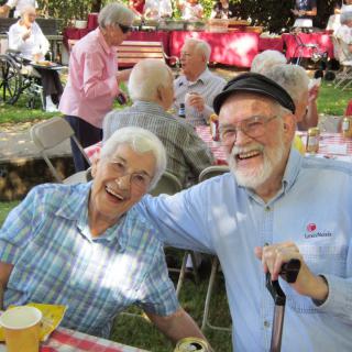 Two seniors smiling and enjoying an outdoor community picnic.