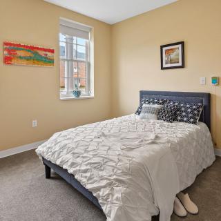 A cozy bedroom with a neatly made bed, artwork on the walls, and a window letting in natural light.
