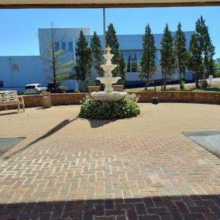 A serene outdoor space featuring a fountain surrounded by trees and benches, under a clear blue sky.