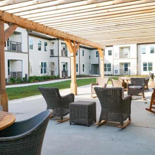 A comfortable outdoor seating area with wicker furniture under a pergola in a residential apartment complex.