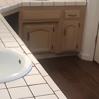 A bathroom with a tiled countertop and a sink, featuring wooden cabinets and flooring.