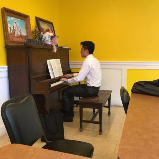 A person in formal attire playing the piano in a room with yellow walls.