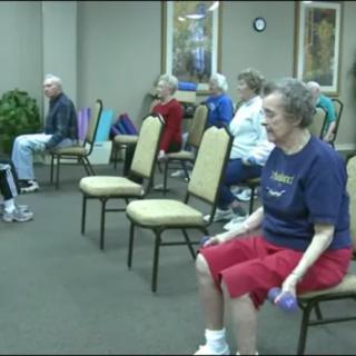 A group of seniors participating in a seated exercise class indoors.