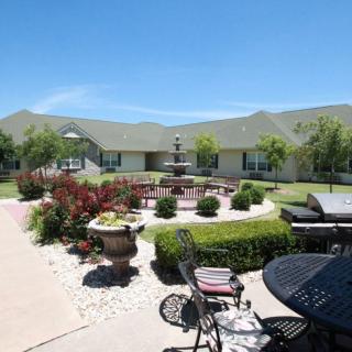 A well-maintained garden with outdoor seating and a building in the background, under a clear blue sky.