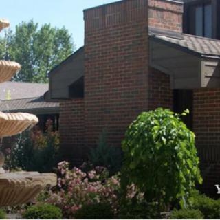 A view of a brick building with an adjacent fountain and landscaped garden.