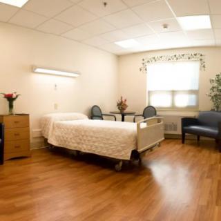A clean and well-furnished hospital room with a bed, chairs, and decorative flowers.