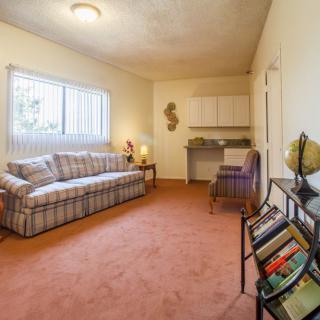 A cozy living room with a sofa, carpeted floor, and a small bookshelf near the window.