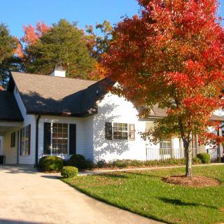 A white house with a driveway surrounded by autumn foliage.