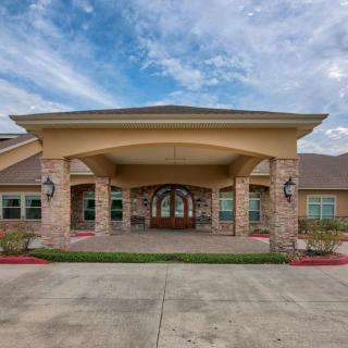 A wide view of a building entrance with an arched driveway and stone pillars under a partly cloudy sky.