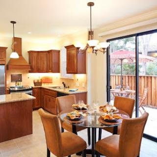 A cozy kitchen and dining area featuring wooden cabinets, a round table set for breakfast, and ample natural light from the sliding door.