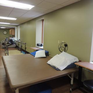 A spacious therapy room equipped with various rehabilitation tools and tables, designed for patient treatment.