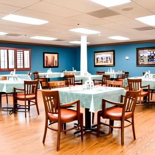 A spacious dining room with neatly arranged tables and chairs, featuring a warm wooden floor and vibrant blue walls adorned with framed pictures.