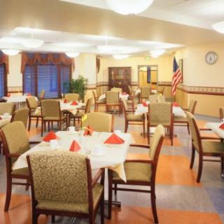 A spacious dining room with neatly arranged tables and chairs, featuring warm lighting and an American flag in the corner.