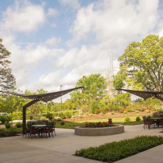A serene outdoor patio with seating areas under curved structures, surrounded by lush greenery and trees.