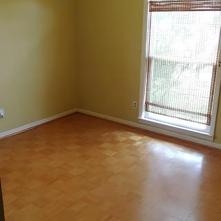 An empty room with yellow walls and a hardwood floor, featuring a window letting in natural sunlight.