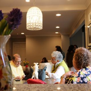 A group of people gathered around a kitchen table, engaged in conversation under a chandelier.