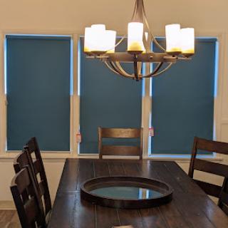 A cozy dining room featuring a wooden table, stylish chairs, and elegant chandelier against blue window shades.