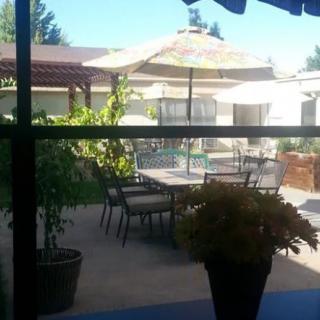 A sunny patio with outdoor furniture, including tables, chairs, and umbrellas, surrounded by plants.