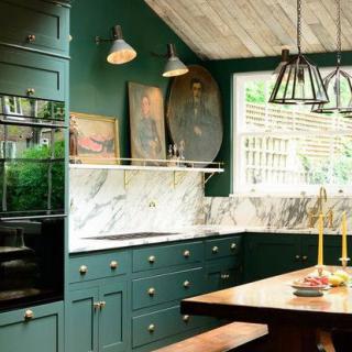 A stylish kitchen with dark green cabinets, a marble backsplash, and modern lighting fixtures.