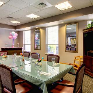 A well-appointed conference room with a glass meeting table, surrounded by chairs and adorned with pink balloons.