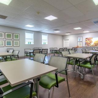 An empty cafeteria with neatly arranged tables and chairs, illuminated by overhead lighting.