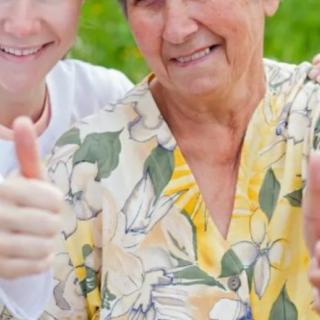 An elderly woman and a young person smiling and giving thumbs up while enjoying their time outdoors.