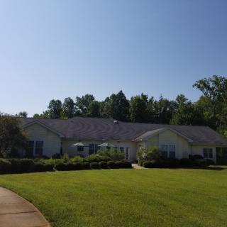 A suburban house with a well-maintained lawn and surrounding trees under a clear blue sky.