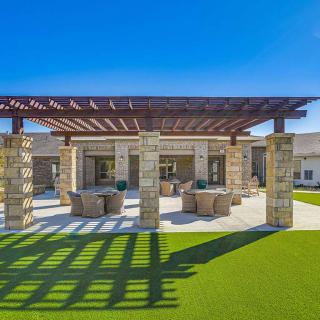 A sunny outdoor patio with a pergola and comfortable seating on a well-maintained lawn.