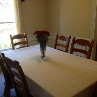 A dining room with a table set for six, featuring a vase with flowers in the center.