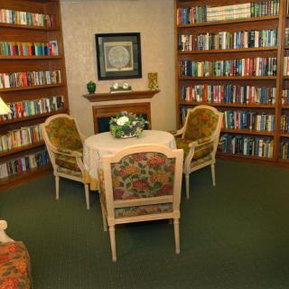 A cozy reading room with bookshelves lining the walls, a round table, and comfortable chairs.