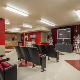 A cozy home theater with a row of cushioned seats facing a large television screen, accented by red and beige decor.