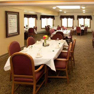 A formal dining room with neatly arranged tables and chairs, set for guests.