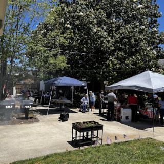 A vibrant outdoor gathering featuring tents and a barbecue setup under a clear blue sky.