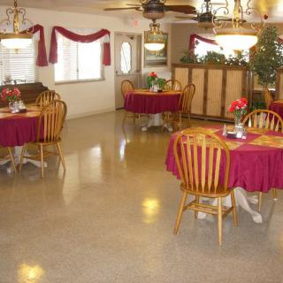 An empty dining area with round tables covered in red tablecloths and wooden chairs.