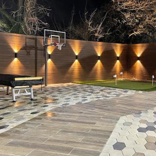 A beautifully lit outdoor space featuring a basketball hoop and elegant landscaping.
