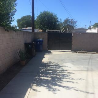 A sunny driveway with trash bins alongside a brick wall and gated entrance.