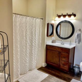 A cozy bathroom with a shower curtain, wooden vanity, and round mirror.