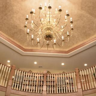A luxurious chandelier hanging from an ornate ceiling above a curved balcony.