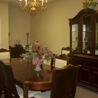 A classic dining room with a wooden table and chairs, a chandelier overhead, and a display cabinet in the background.