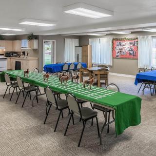 A multi-purpose event room set up with tables and chairs, featuring green tablecloths and a small kitchenette.