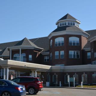 A large, multi-story brick building with a distinctive roof and parked cars in front.