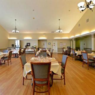 An elegant dining room with neatly arranged tables and chairs, featuring chandeliers and a wooden floor.