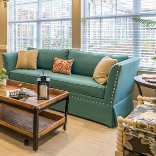 A cozy living room with a teal sofa and a wooden coffee table in front of large windows.